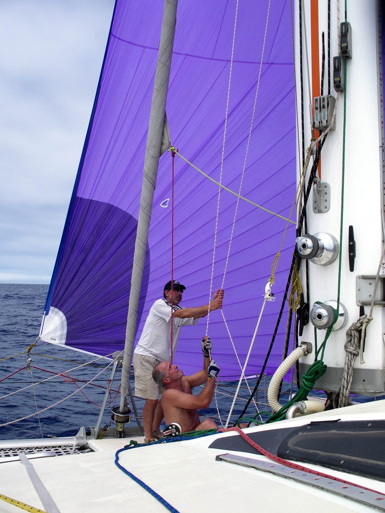 Two men hoist a blue sail